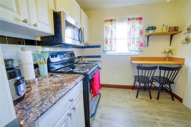 kitchen featuring backsplash, stainless steel appliances, white cabinets, light tile patterned flooring, and dark stone counters