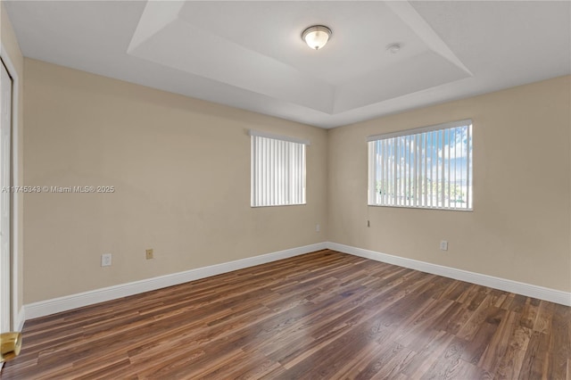 empty room with dark hardwood / wood-style flooring and a tray ceiling