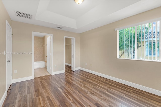 unfurnished bedroom with connected bathroom, a spacious closet, a raised ceiling, a closet, and hardwood / wood-style floors