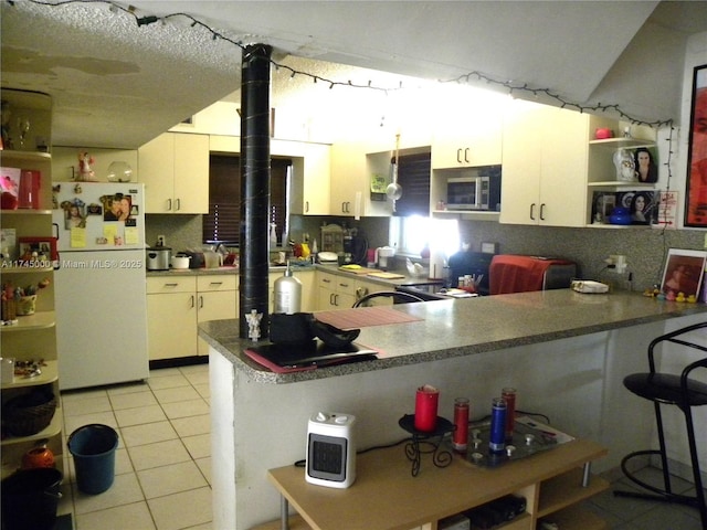 kitchen with white refrigerator, light tile patterned flooring, white cabinets, and kitchen peninsula