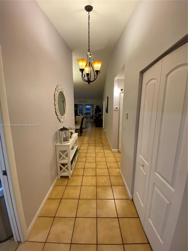 corridor featuring light tile patterned floors, baseboards, and an inviting chandelier