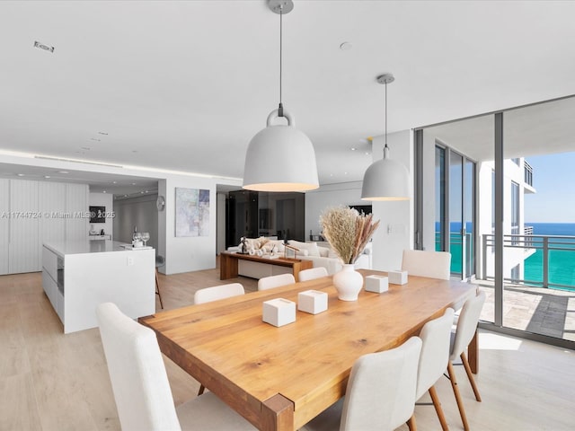 dining area featuring light wood-style floors, floor to ceiling windows, and a water view
