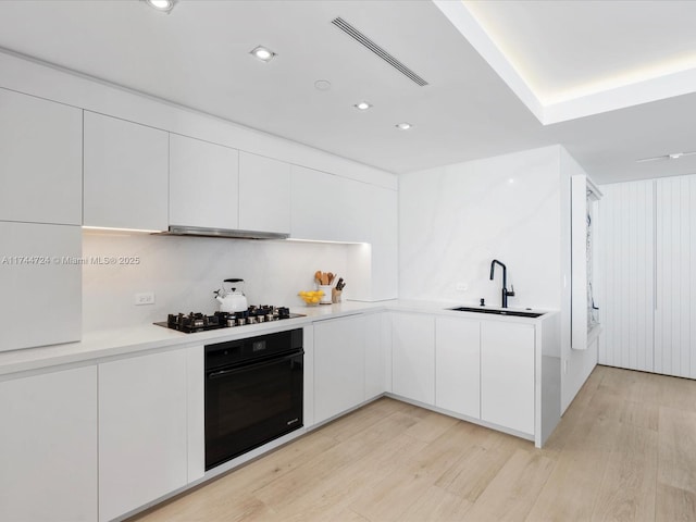 kitchen with black appliances, white cabinetry, light countertops, and a sink