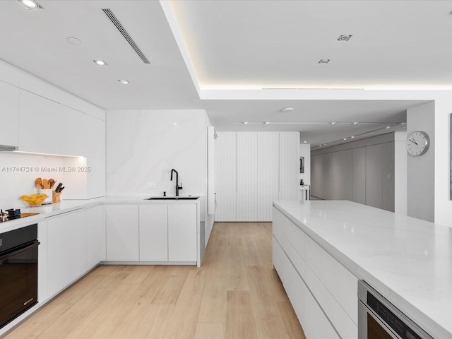 kitchen featuring light wood finished floors, white cabinets, modern cabinets, black appliances, and a sink