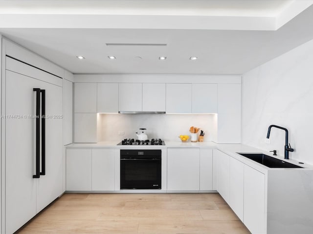 kitchen featuring white cabinets, light countertops, a sink, and black appliances