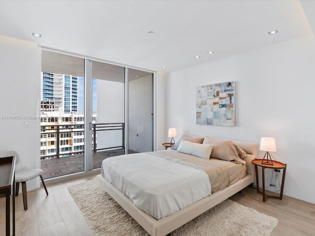 bedroom featuring a view of city, light wood finished floors, recessed lighting, expansive windows, and access to outside