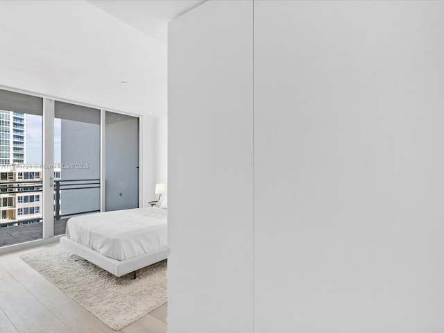 bedroom with expansive windows, access to outside, a city view, and light wood finished floors