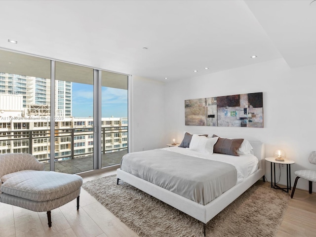 bedroom with wood finished floors, access to outside, expansive windows, a view of city, and recessed lighting