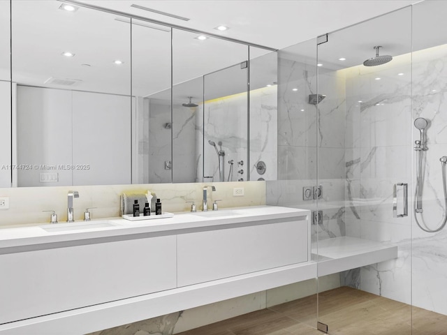 bathroom with double vanity, a marble finish shower, decorative backsplash, and a sink