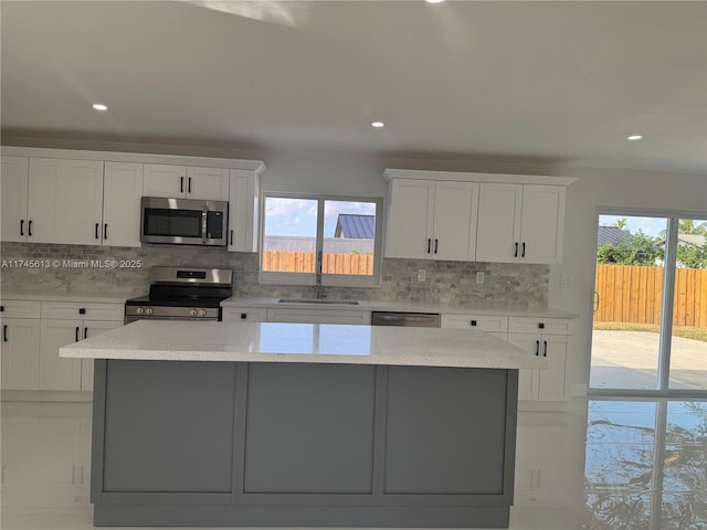 kitchen featuring stainless steel appliances, a wealth of natural light, a kitchen island, and white cabinets