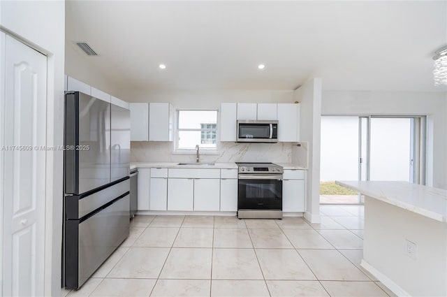 kitchen featuring white cabinetry, sink, backsplash, light tile patterned floors, and stainless steel appliances