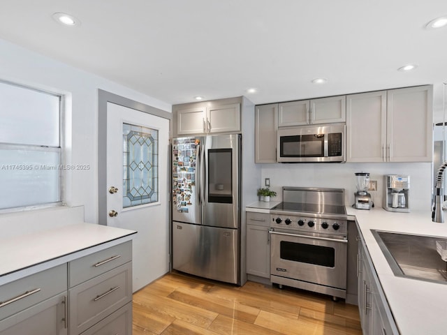 kitchen with gray cabinets, appliances with stainless steel finishes, light countertops, and light wood-style flooring