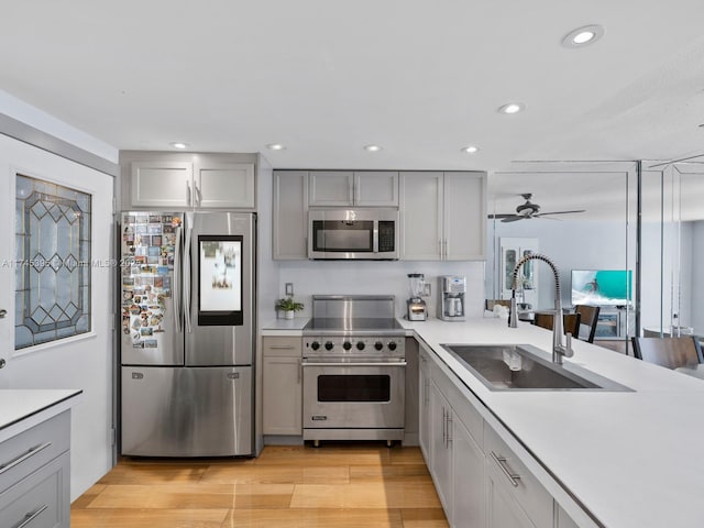 kitchen featuring ceiling fan, light countertops, gray cabinets, stainless steel appliances, and a sink