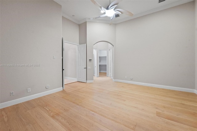 spare room featuring crown molding, ceiling fan, a towering ceiling, and light wood-type flooring