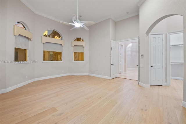 spare room featuring a towering ceiling, light hardwood / wood-style flooring, ornamental molding, and ceiling fan