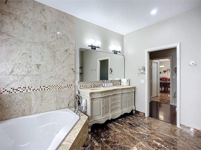 bathroom with vanity, a textured ceiling, and tiled tub