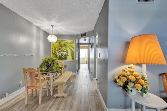 hallway with light hardwood / wood-style floors, a chandelier, and a textured ceiling