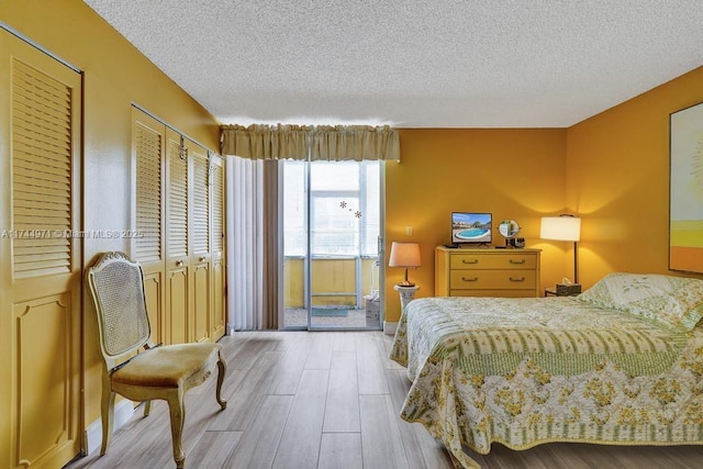 bedroom with a textured ceiling, multiple closets, and light wood-type flooring