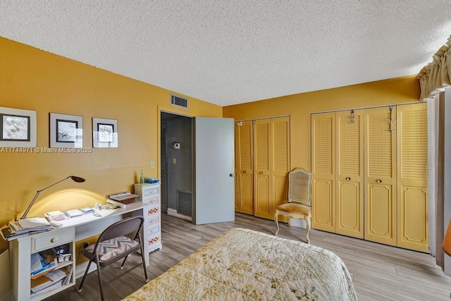 bedroom with two closets, a textured ceiling, and light wood-type flooring