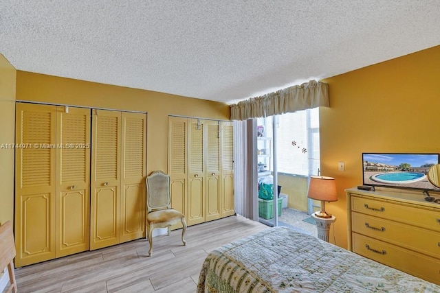 bedroom with two closets, a textured ceiling, and light hardwood / wood-style floors