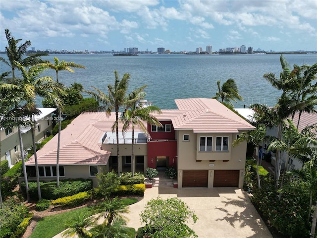 exterior space with stucco siding, a tiled roof, an attached garage, a water view, and driveway