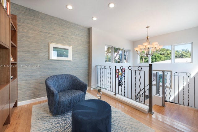 living area featuring a notable chandelier, an accent wall, recessed lighting, baseboards, and an upstairs landing