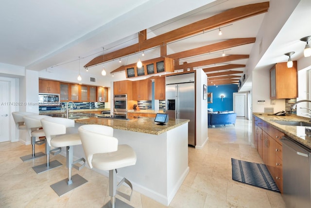 kitchen with glass insert cabinets, brown cabinets, rail lighting, a sink, and appliances with stainless steel finishes