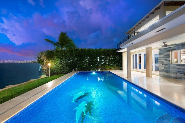 pool at dusk with ceiling fan, a patio area, and an outdoor pool