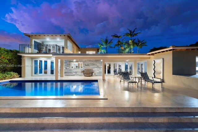 rear view of house with french doors, an outdoor pool, a balcony, a patio, and stucco siding