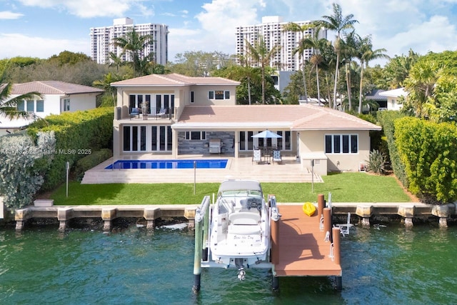 rear view of property with boat lift, an outdoor pool, a water view, a balcony, and a yard