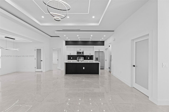 kitchen featuring appliances with stainless steel finishes, pendant lighting, white cabinetry, a tray ceiling, and a center island with sink