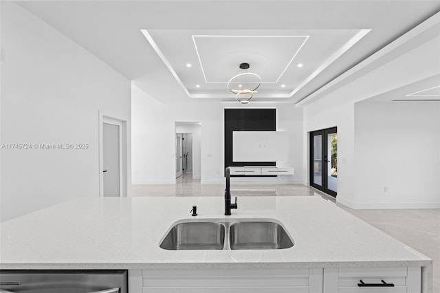 kitchen featuring a towering ceiling, sink, white cabinets, a tray ceiling, and light stone countertops