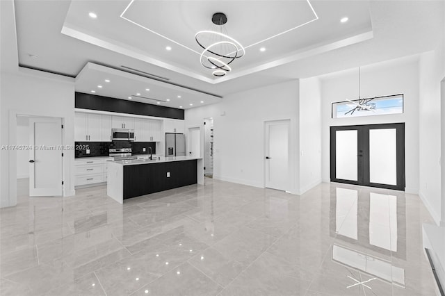 kitchen featuring hanging light fixtures, an island with sink, appliances with stainless steel finishes, and a raised ceiling