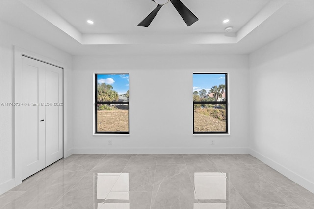 unfurnished bedroom with multiple windows, ceiling fan, and a tray ceiling