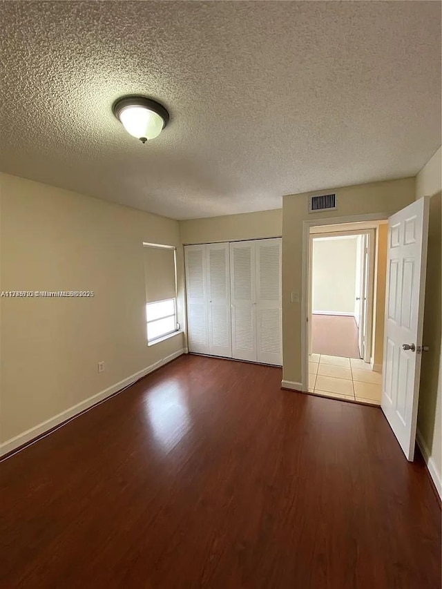 unfurnished bedroom with dark hardwood / wood-style floors, a textured ceiling, and a closet