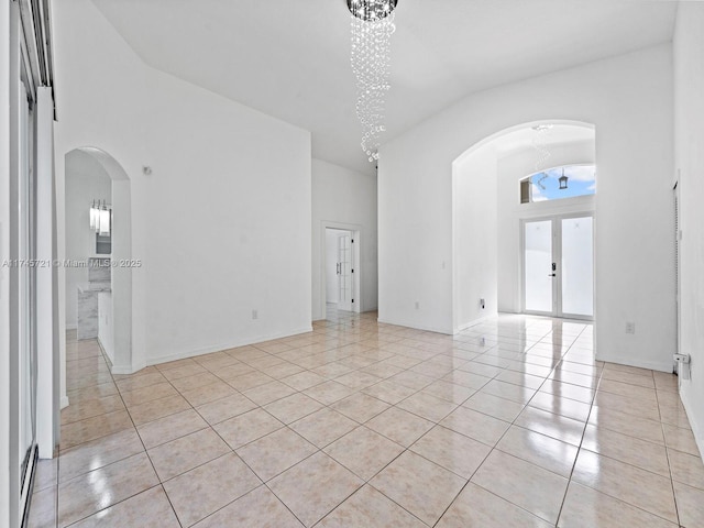 tiled spare room featuring a chandelier, high vaulted ceiling, and french doors