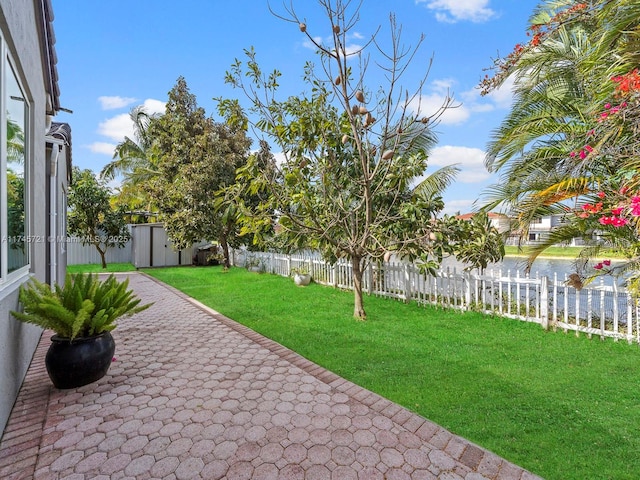 view of yard featuring a storage shed, a patio, and a water view