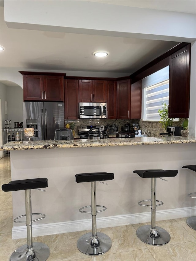 kitchen with tasteful backsplash, light stone countertops, a kitchen breakfast bar, and appliances with stainless steel finishes