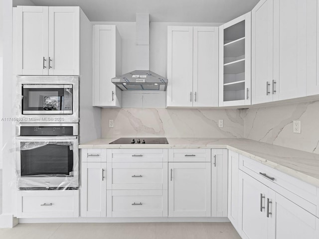 kitchen featuring wall chimney exhaust hood, stainless steel appliances, decorative backsplash, glass insert cabinets, and light stone counters