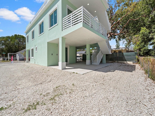 back of property with a balcony, a carport, fence, stucco siding, and stairs
