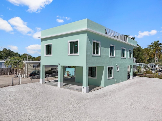 rear view of house with gravel driveway, a patio, a carport, and fence