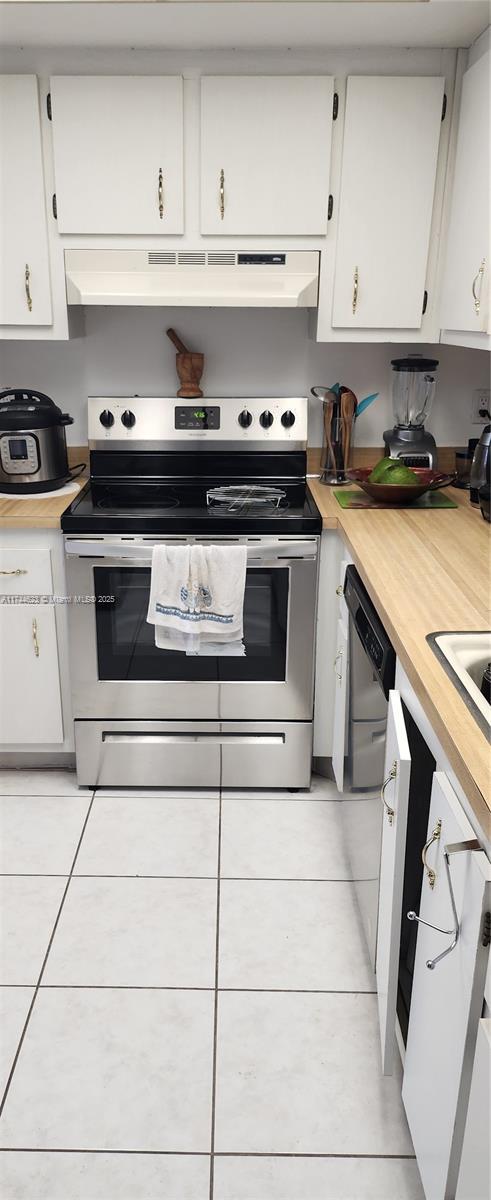 kitchen with appliances with stainless steel finishes, light tile patterned flooring, white cabinetry, and under cabinet range hood