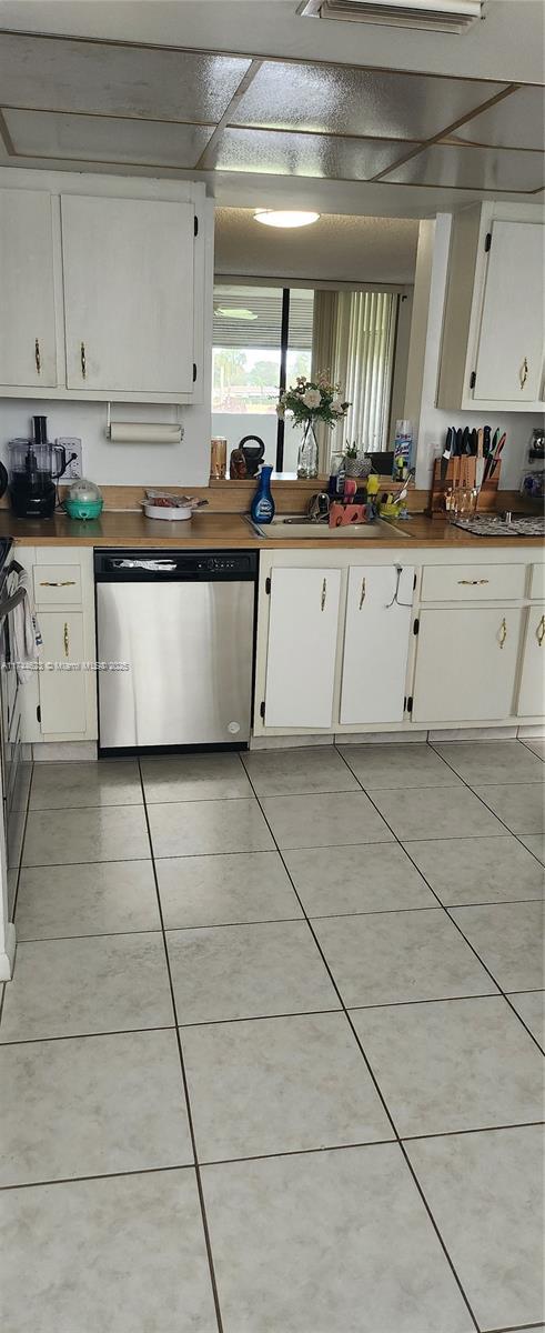 kitchen with light tile patterned floors, dark countertops, white cabinets, a sink, and dishwasher