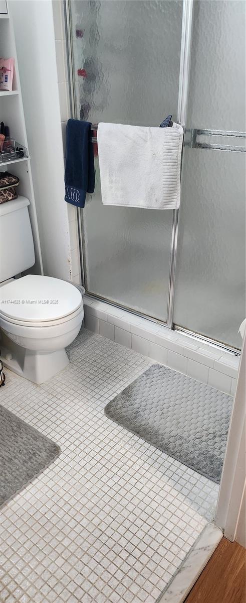 full bath with toilet, a stall shower, and tile patterned floors