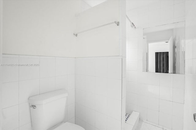 bathroom with toilet, a tile shower, and tile walls