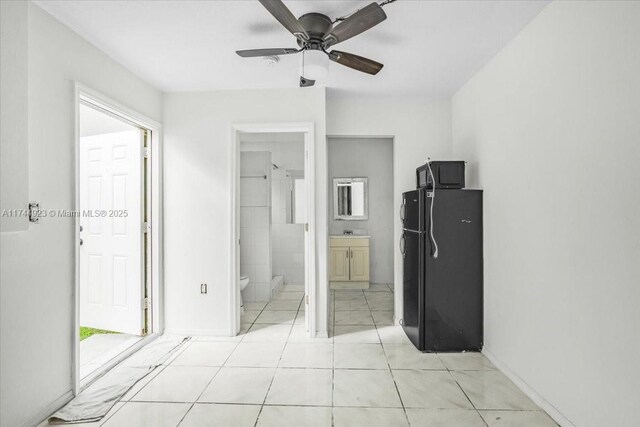 unfurnished bedroom featuring connected bathroom, freestanding refrigerator, light tile patterned floors, ceiling fan, and a sink