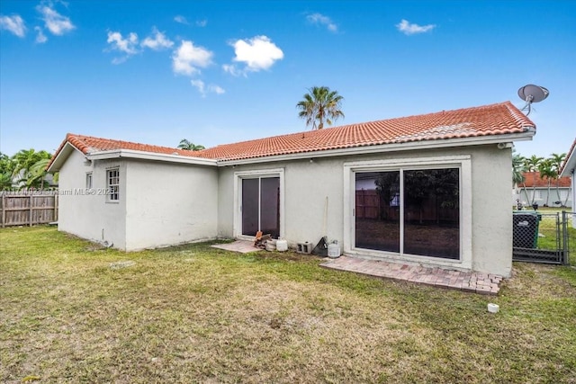rear view of house with a lawn, stucco siding, a tiled roof, and fence