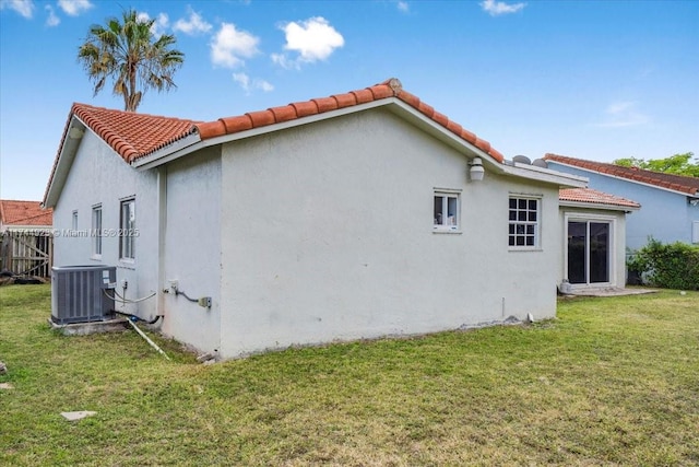 view of property exterior featuring stucco siding, a tile roof, a yard, and central air condition unit