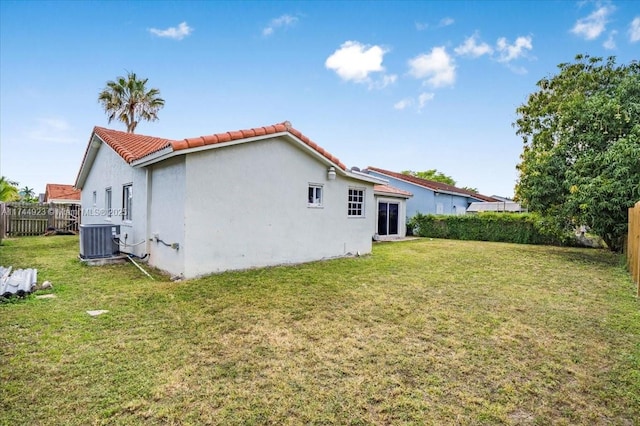 back of property featuring central AC, fence, a tile roof, and a yard