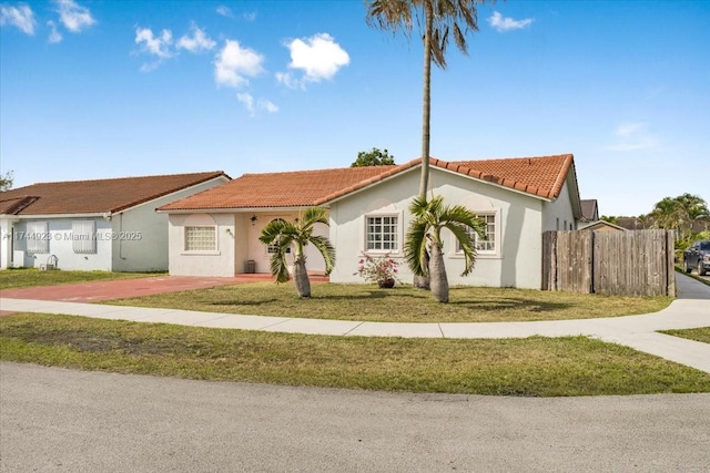 view of front facade with fence, a tiled roof, a front yard, and stucco siding